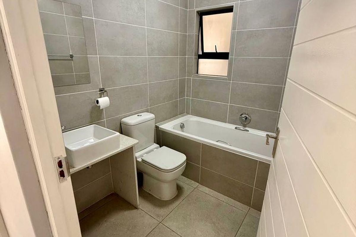A modern, well-maintained bathroom featuring floor-to-ceiling grey tiling, a built-in bathtub, a contemporary vessel sink, and a toilet.