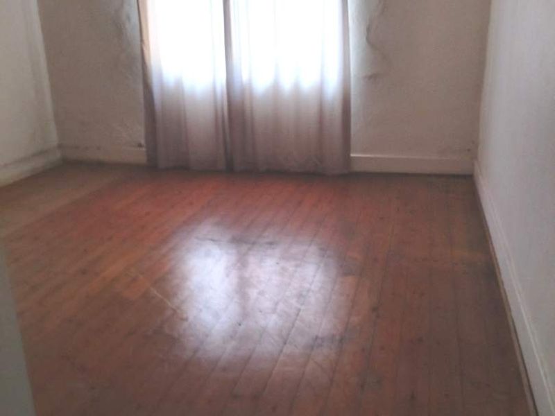 An empty bedroom featuring original timber flooring and a window, requiring cosmetic updates to the walls and floor finish.