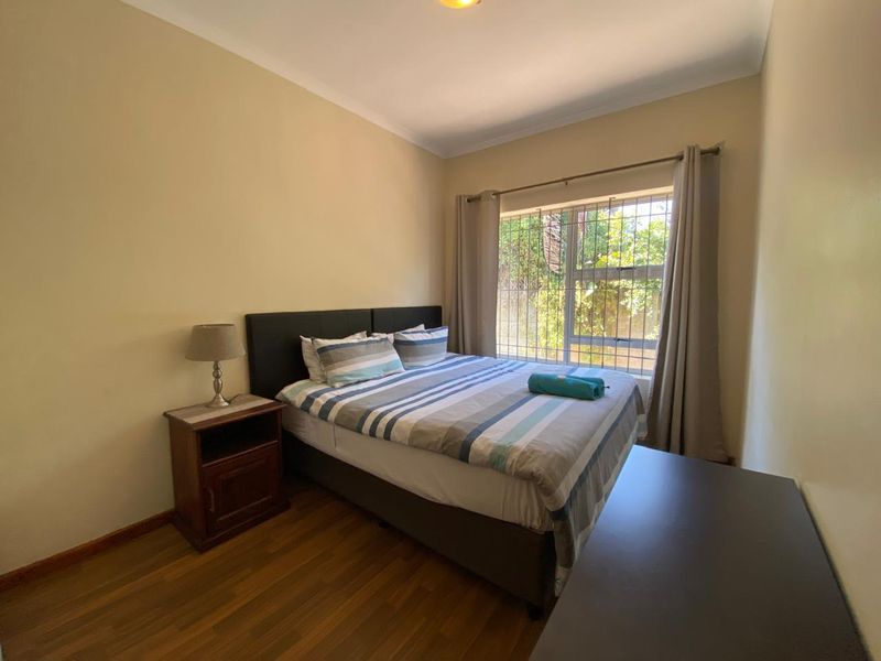 A standard bedroom featuring laminate flooring, neutral wall paint, and a window fitted with security bars.