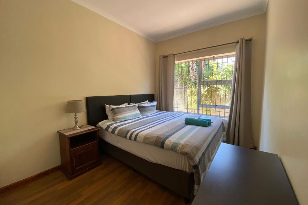 A standard bedroom featuring laminate flooring, neutral wall paint, and a window fitted with security bars.