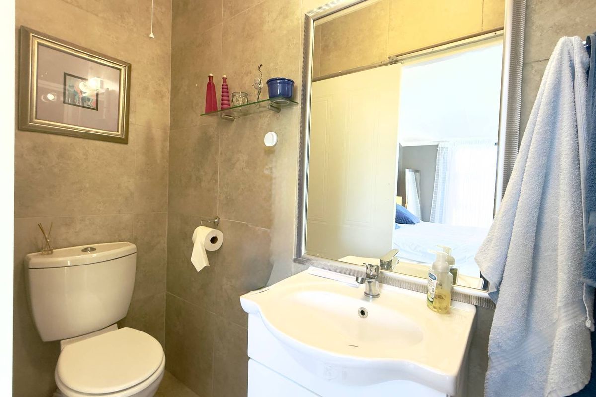 A compact bathroom featuring neutral wall tiling, a modern vanity basin with mixer tap, and a large wall-mounted mirror.