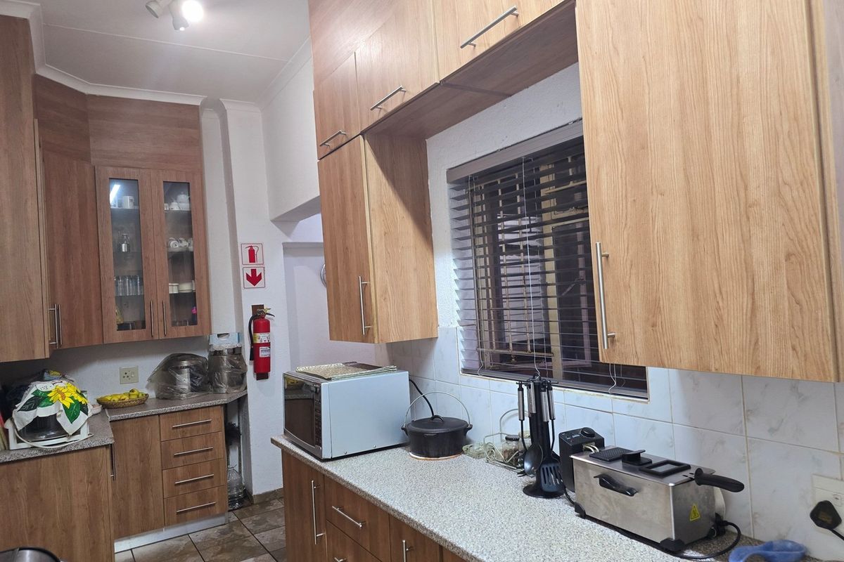 Functional kitchen featuring wood-look cabinetry, stone-style countertops, tiled backsplash, and a window with fitted blinds.