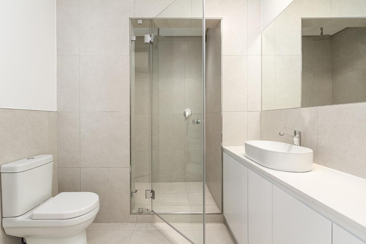 Modern bathroom featuring a walk-in glass shower, wall-mounted toilet, and a sleek vanity with a vessel sink and large mirror.