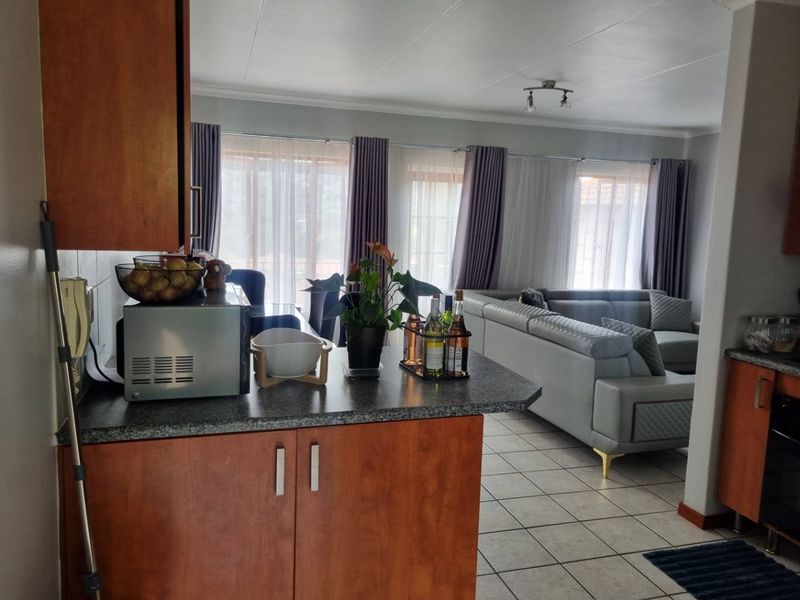 Open-plan living and kitchen area featuring tiled flooring, wooden cabinetry, and direct access to a patio through large glass sliding doors.