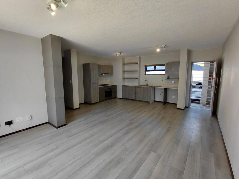 Spacious open-plan living area featuring modern laminate flooring, a functional kitchen with built-in cabinetry, oven, hob, and direct access to the exterior.