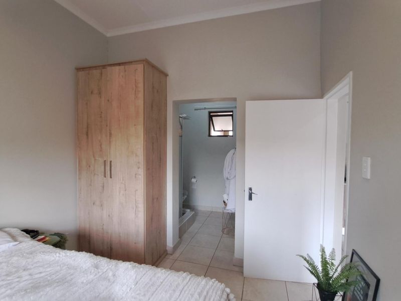 A well-maintained bedroom featuring neutral wall tones, tiled flooring, and a built-in wardrobe, with direct access to an adjoining bathroom.