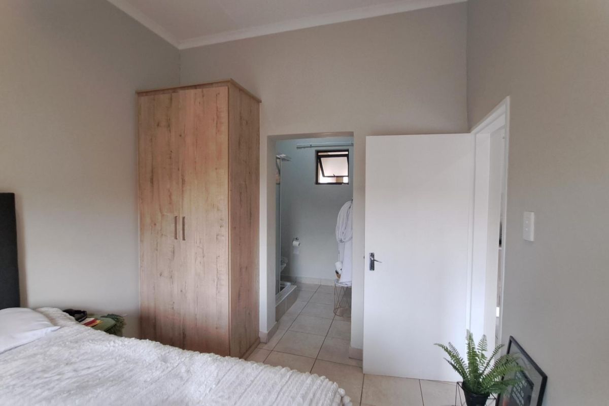 A well-maintained bedroom featuring neutral wall tones, tiled flooring, and a built-in wardrobe, with direct access to an adjoining bathroom.