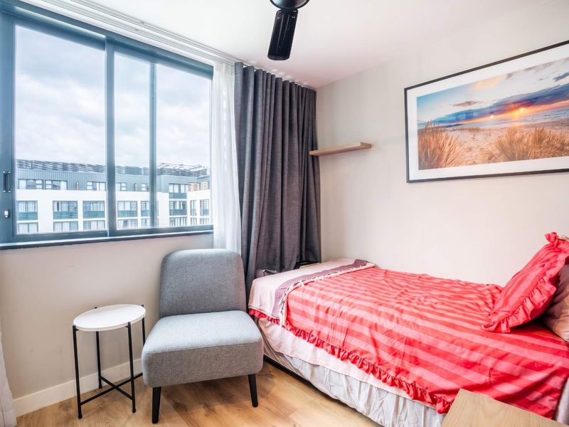 A well-lit bedroom featuring laminate flooring, a ceiling fan, and a large sliding window providing natural light and urban views.