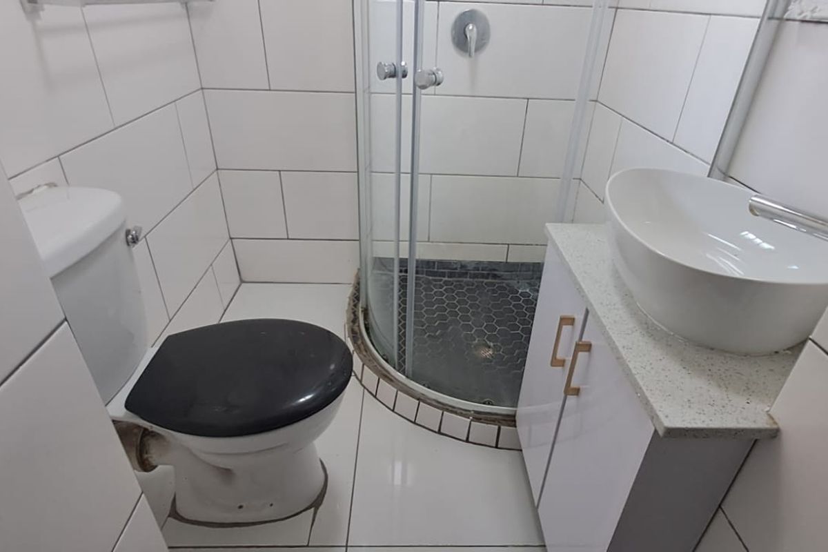 Compact modern bathroom featuring a corner shower enclosure, white vanity with vessel sink, and full-height wall tiling.