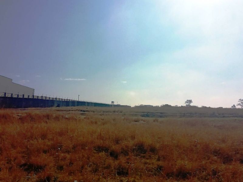 A wide view of a vacant commercial land plot featuring dry grass and perimeter security fencing along the boundary.