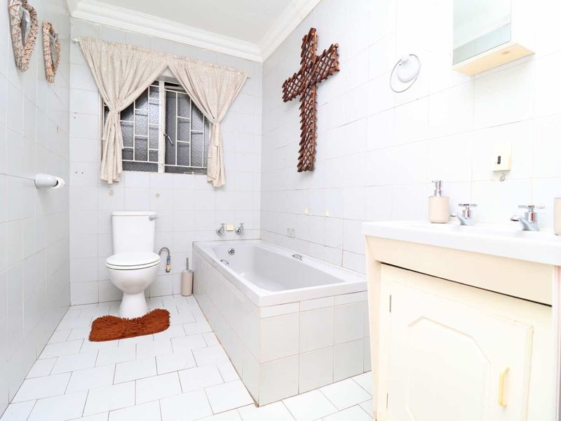 A dated bathroom featuring a built-in bathtub, toilet, and vanity cabinet with tiled finishes throughout.