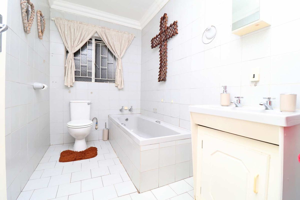 A dated bathroom featuring a built-in bathtub, toilet, and vanity cabinet with tiled finishes throughout.