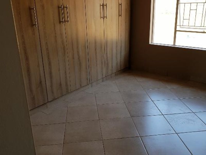 A bright, empty bedroom featuring neutral tiled flooring and extensive built-in wooden cupboards, offering ample storage space.