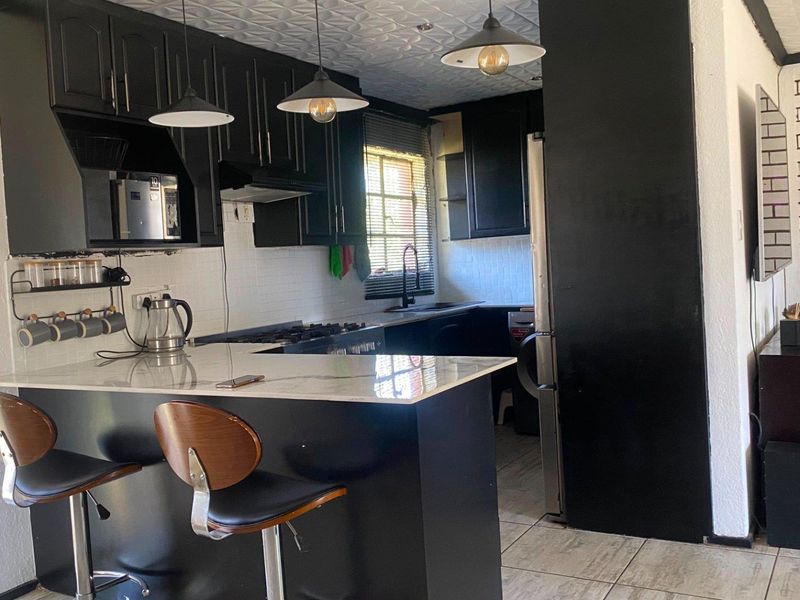 Modern kitchen featuring black cabinetry, stone countertops, a breakfast bar, and an exposed brick feature wall, creating a stylish and functional cooking space.