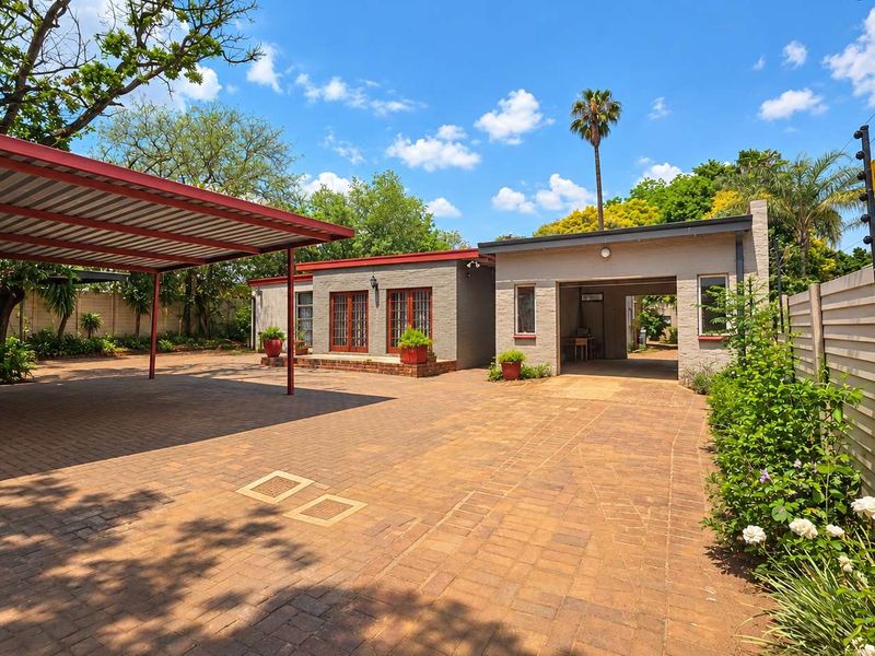 Front exterior view featuring a spacious paved driveway, a covered carport, and a brick-finished building with classic french doors.