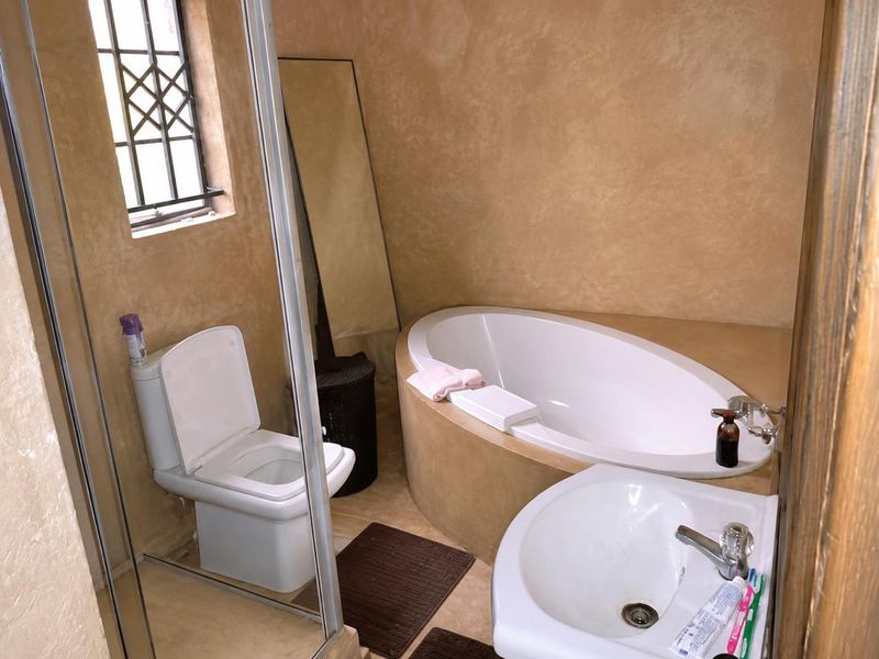 A compact bathroom featuring a built-in oval bathtub, pedestal basin, and toilet, finished with textured wall treatments and security bars on the window.