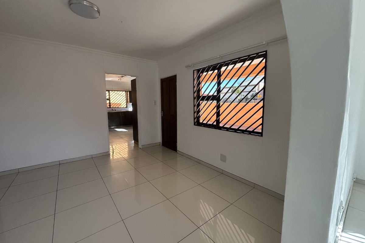 A bright, empty living area featuring neutral tiled flooring, an arched entryway, and a window fitted with security bars.