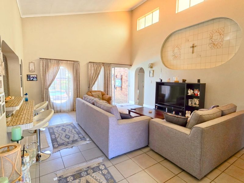 Spacious living room featuring high vaulted ceilings, tiled flooring, a built-in decorative wall niche, and a breakfast bar area with access to the patio.