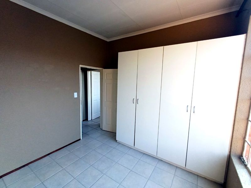A spacious bedroom featuring neutral wall tones, tiled flooring, and ample built-in cupboard storage, offering a clean and functional living space.