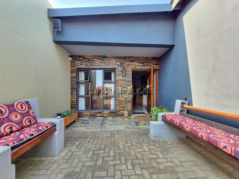 A covered patio area featuring stone cladding, paved flooring, and built-in concrete seating, providing a functional outdoor entertainment space.