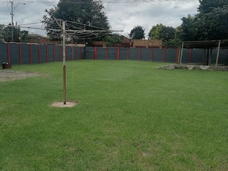 A spacious backyard featuring a large lawn, perimeter walling, a rotary clothesline, and a covered outdoor structure.