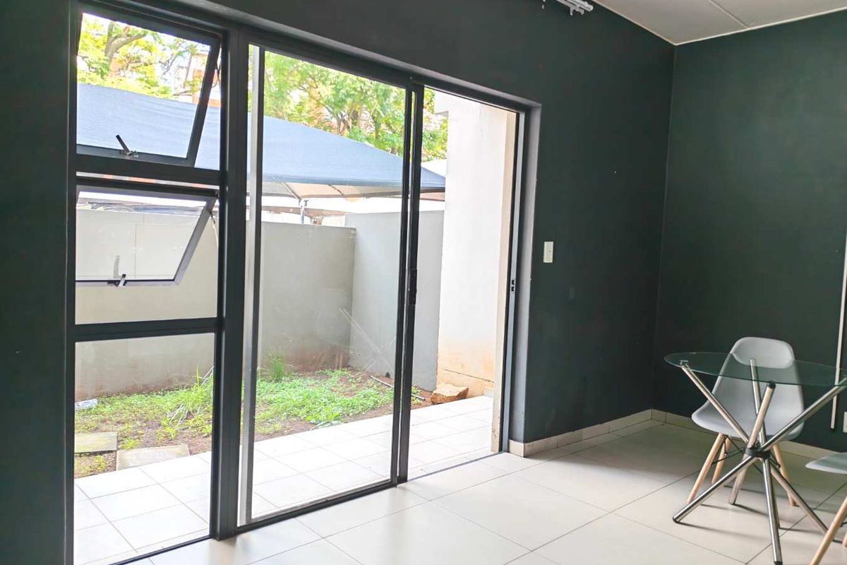 A bright living area featuring large sliding glass doors that open onto a private patio and garden space, finished with neutral floor tiles.