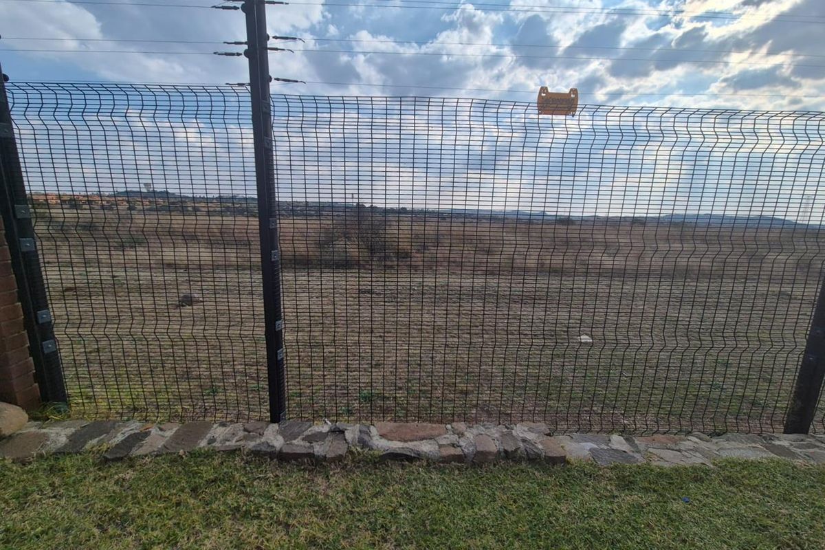 View of the property boundary featuring a secure wire mesh fence with electric fencing and a stone-edged lawn.