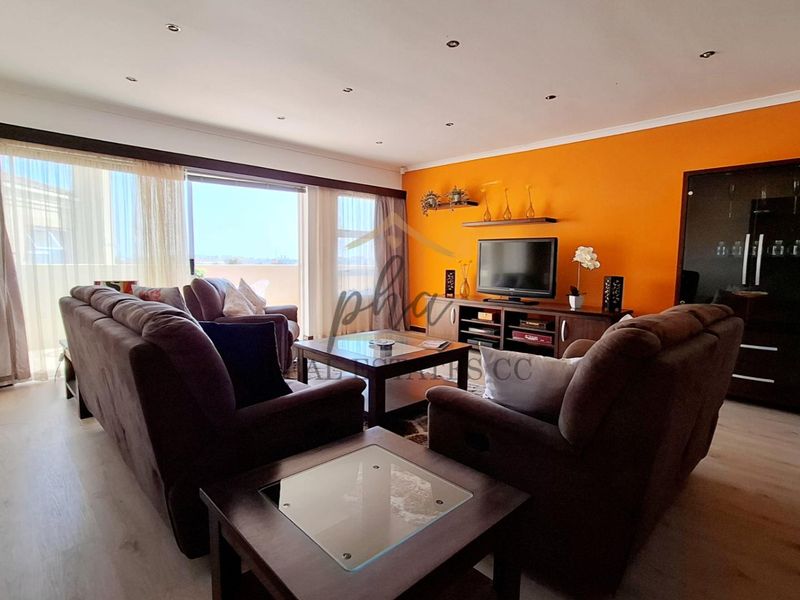 Spacious living room featuring laminate flooring, recessed downlighting, and large sliding glass doors providing access to the balcony.