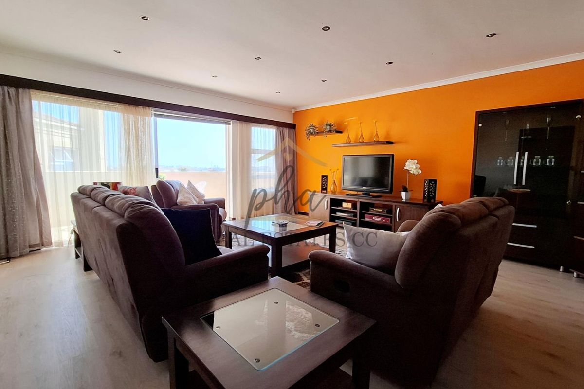 Spacious living room featuring laminate flooring, recessed downlighting, and large sliding glass doors providing access to the balcony.