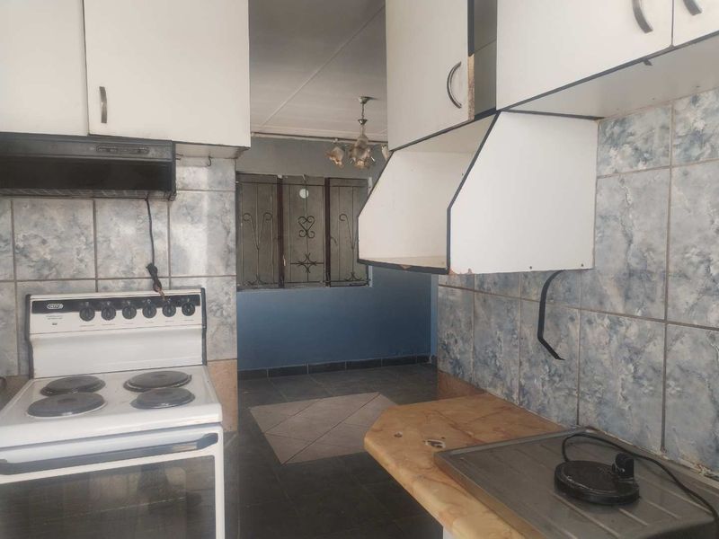 A dated kitchen featuring built-in cabinetry, a freestanding stove, and tiled splashbacks, offering potential for a modern renovation.