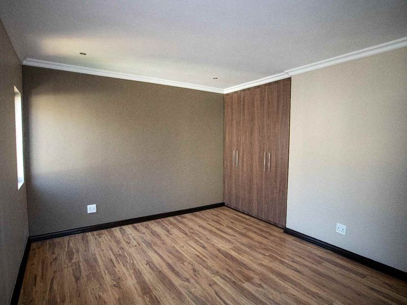 A clean, empty bedroom featuring modern laminate flooring, neutral wall tones, and built-in wooden cupboards with recessed ceiling lighting.