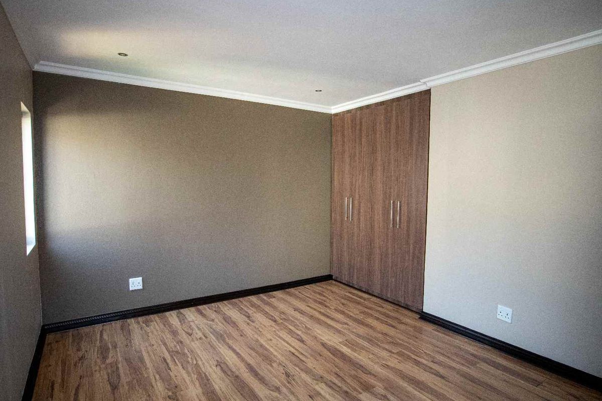 A clean, empty bedroom featuring modern laminate flooring, neutral wall tones, and built-in wooden cupboards with recessed ceiling lighting.