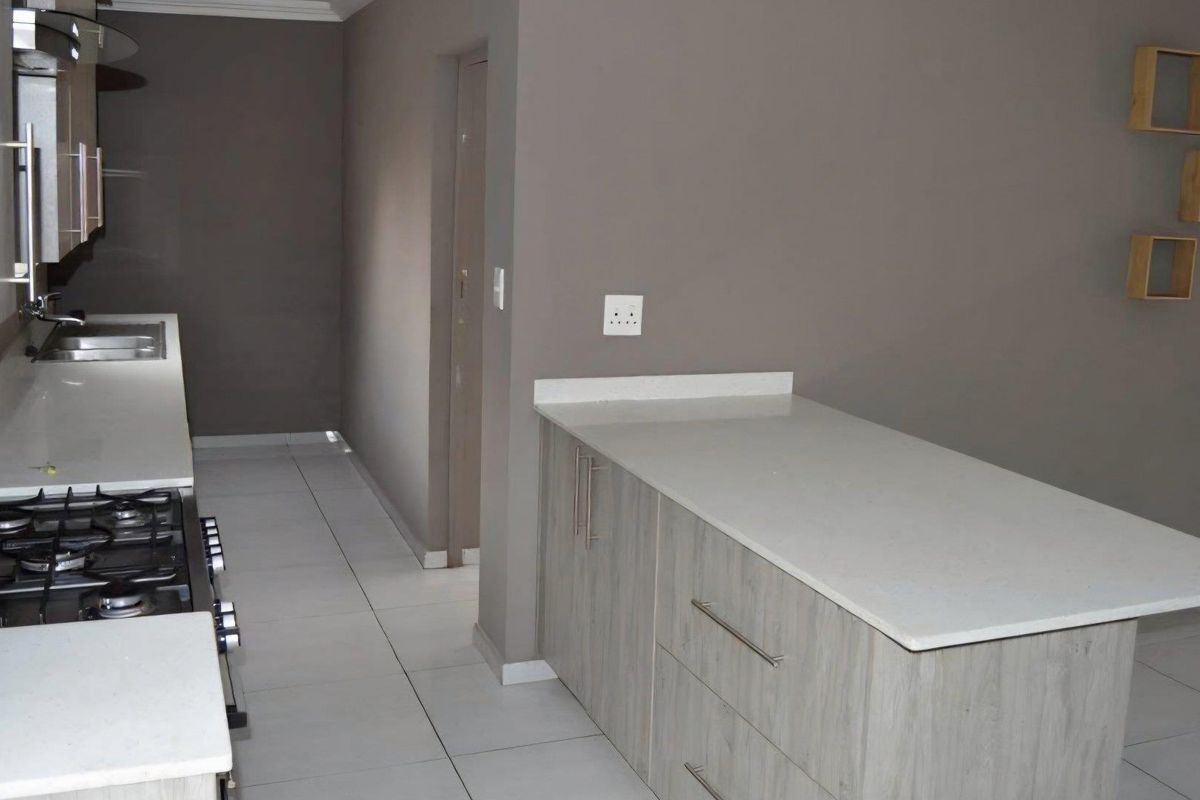 Modern kitchen featuring light wood cabinetry, stone countertops, a built-in gas hob, and tiled flooring in an open-plan layout.