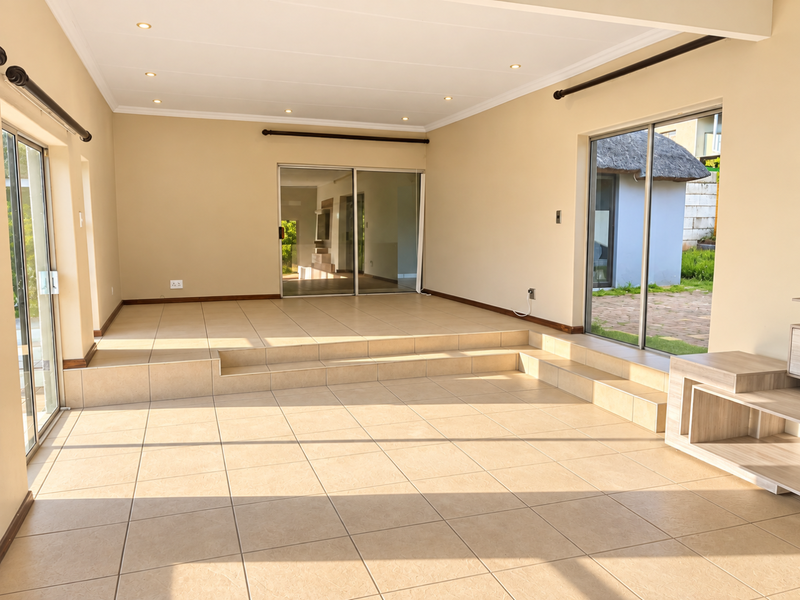 Spacious, sunlit living area featuring neutral tiled flooring, a raised platform level, and multiple sliding glass doors providing seamless indoor-outdoor flow.