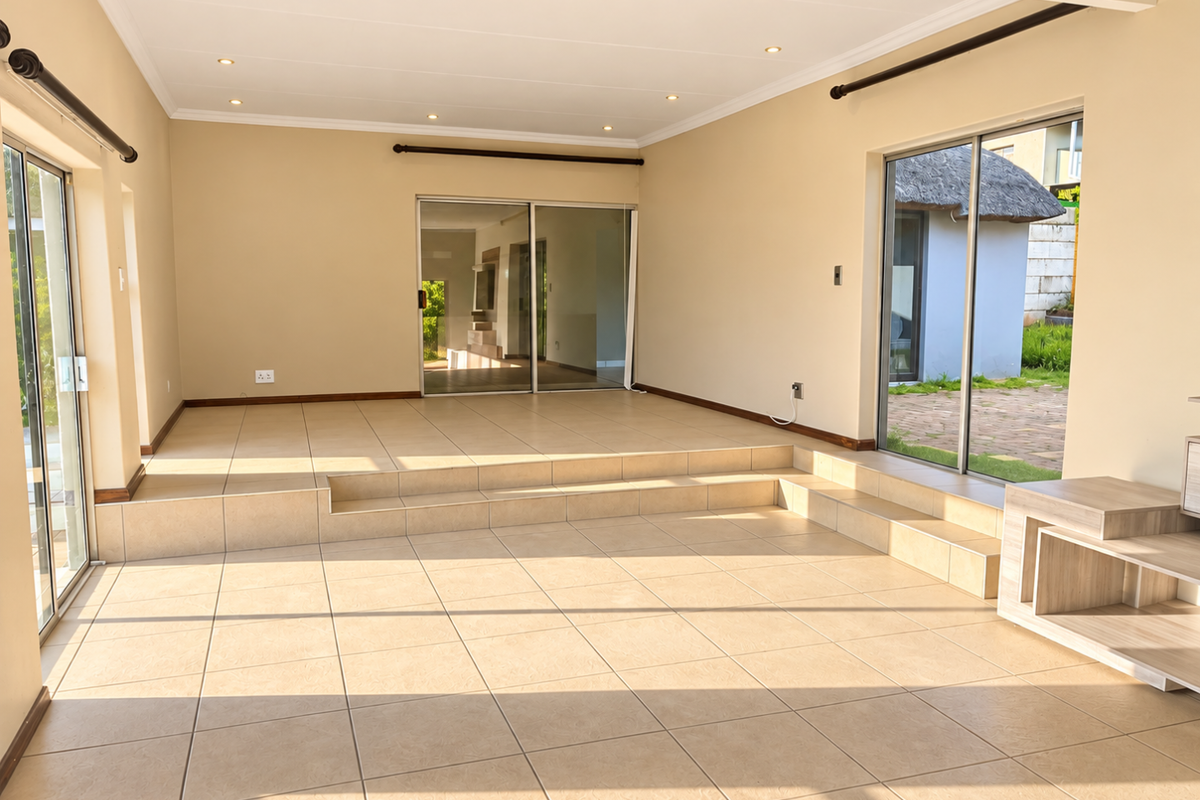 Spacious, sunlit living area featuring neutral tiled flooring, a raised platform level, and multiple sliding glass doors providing seamless indoor-outdoor flow.