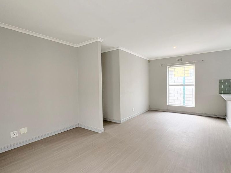 A bright and spacious open-plan living area featuring neutral walls, modern laminate flooring, and a functional kitchen counter with a tiled splashback.