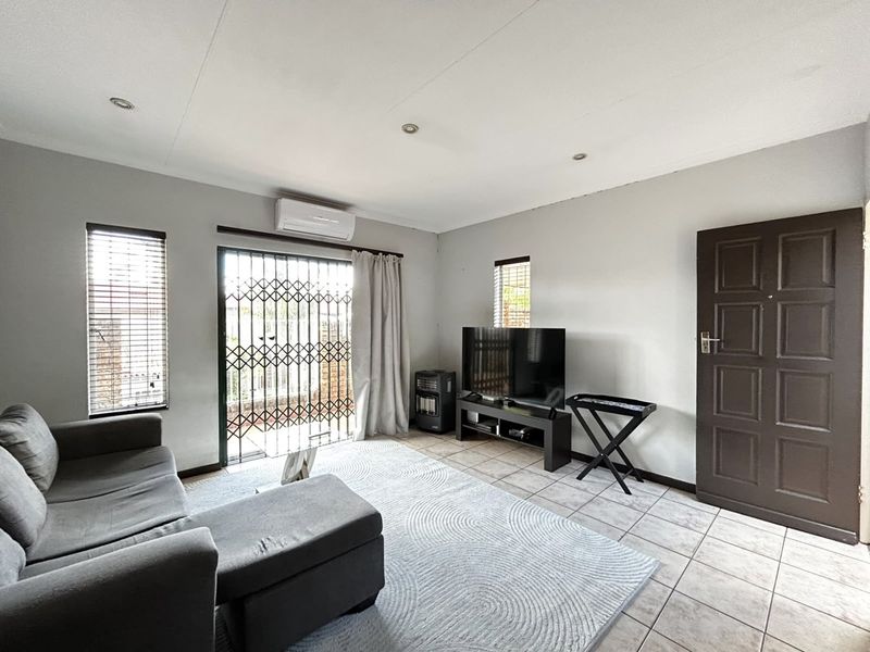 A functional living room featuring tiled flooring, recessed lighting, a split-system air conditioner, and a sliding glass door with a security gate.