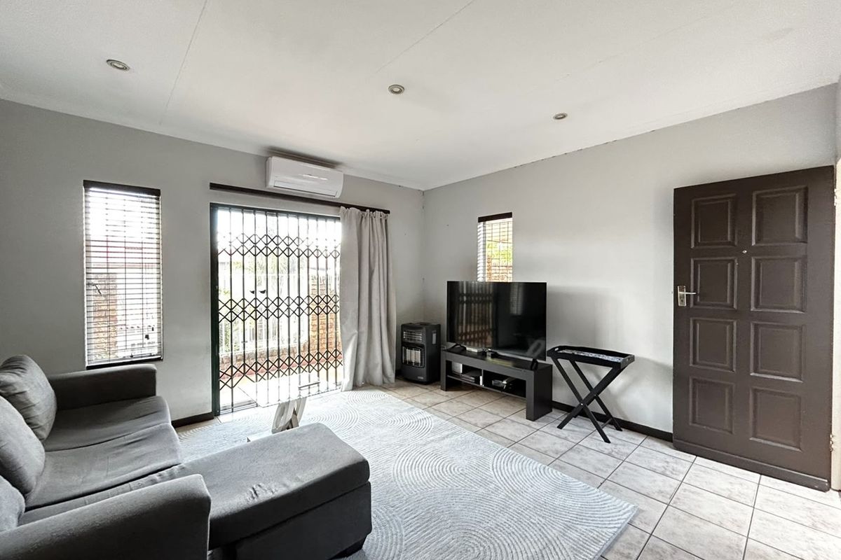 A functional living room featuring tiled flooring, recessed lighting, a split-system air conditioner, and a sliding glass door with a security gate.