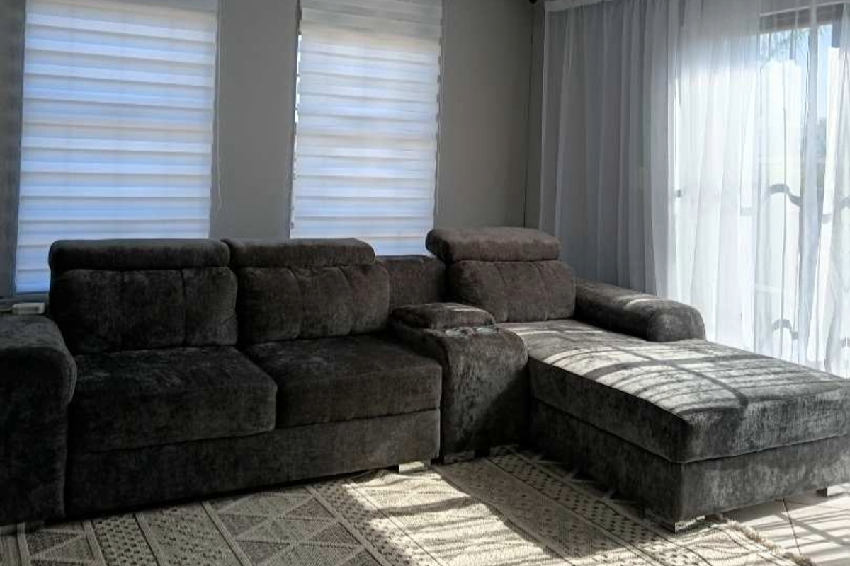 A bright living room featuring tiled flooring, modern roller blinds, and sheer curtains, providing a comfortable and well-lit space.