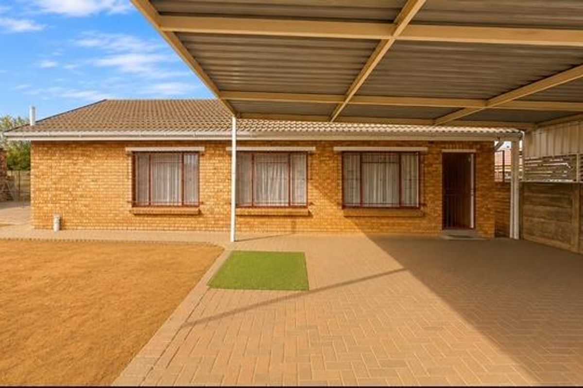 Rear view of a brick house featuring a large paved carport area, tiled roof, and secure window bars.