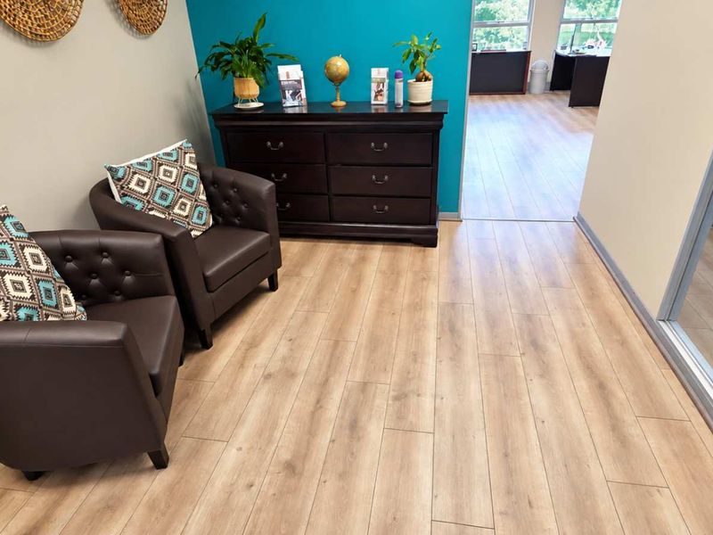 A professional office reception area featuring modern laminate flooring, a glass partition wall, and a vibrant teal accent wall.