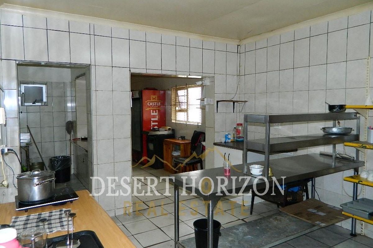 Commercial kitchen area featuring tiled walls and floors, stainless steel prep tables, and an adjoining scullery or storage space.