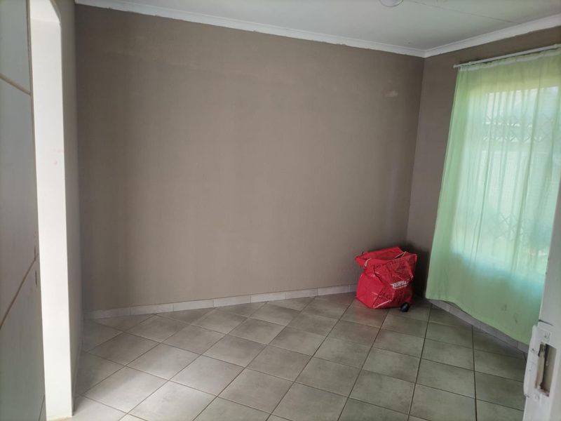 A simple, empty bedroom featuring neutral wall paint, ceramic floor tiles, and a window fitted with a security gate.