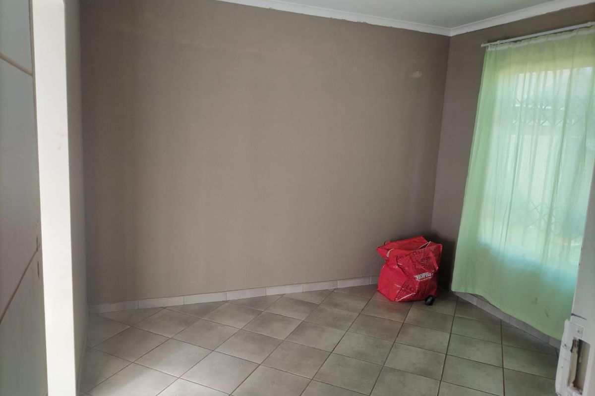 A simple, empty bedroom featuring neutral wall paint, ceramic floor tiles, and a window fitted with a security gate.