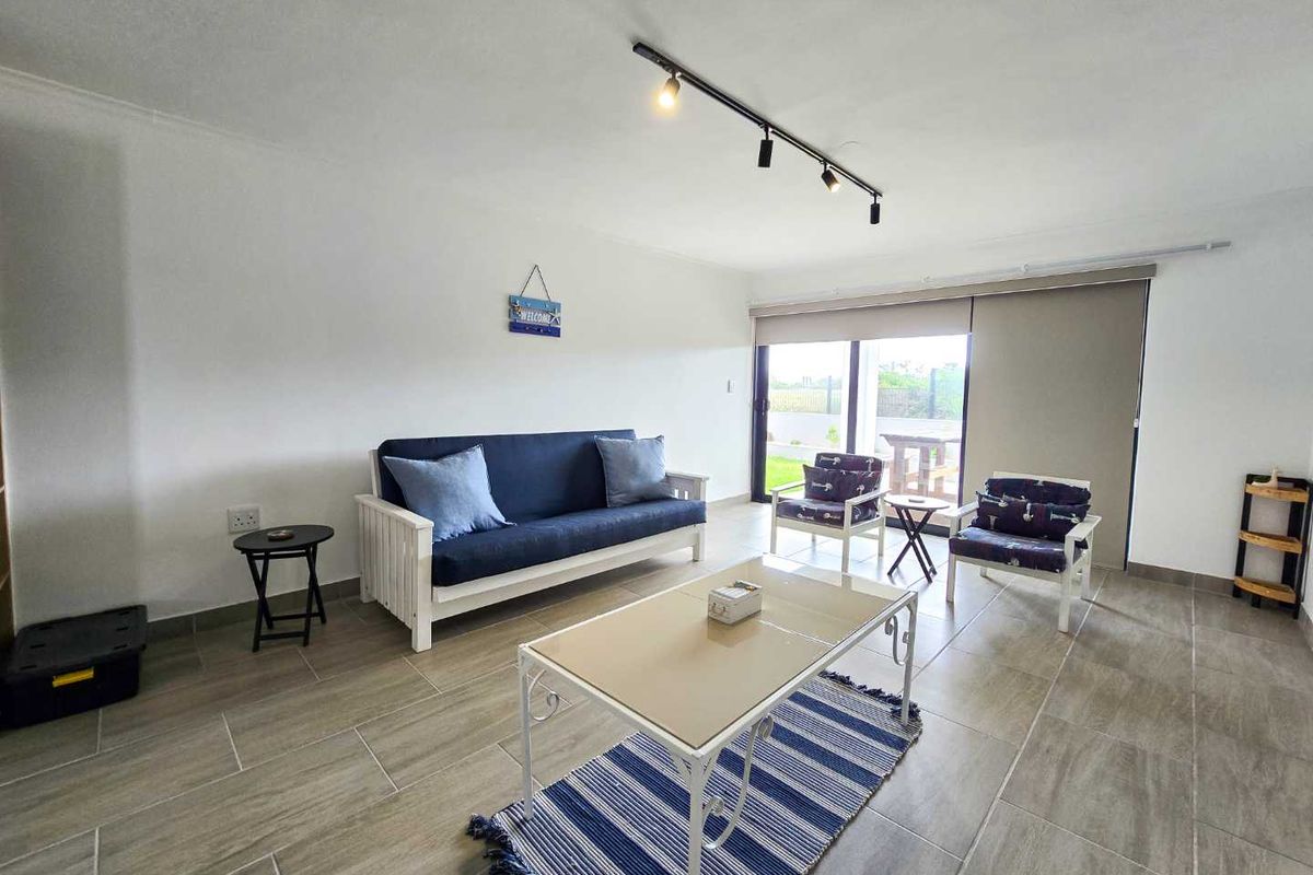 A bright and spacious living room featuring large sliding glass doors that open to an outdoor patio area, finished with neutral floor tiles.