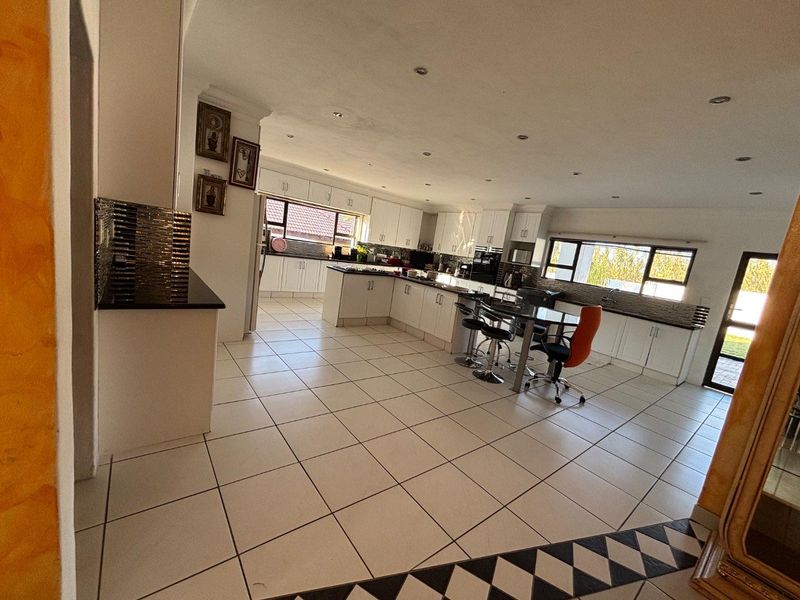 Spacious open-plan kitchen featuring white cabinetry, granite countertops, tiled flooring, and recessed lighting, offering a functional layout for cooking and casual dining.