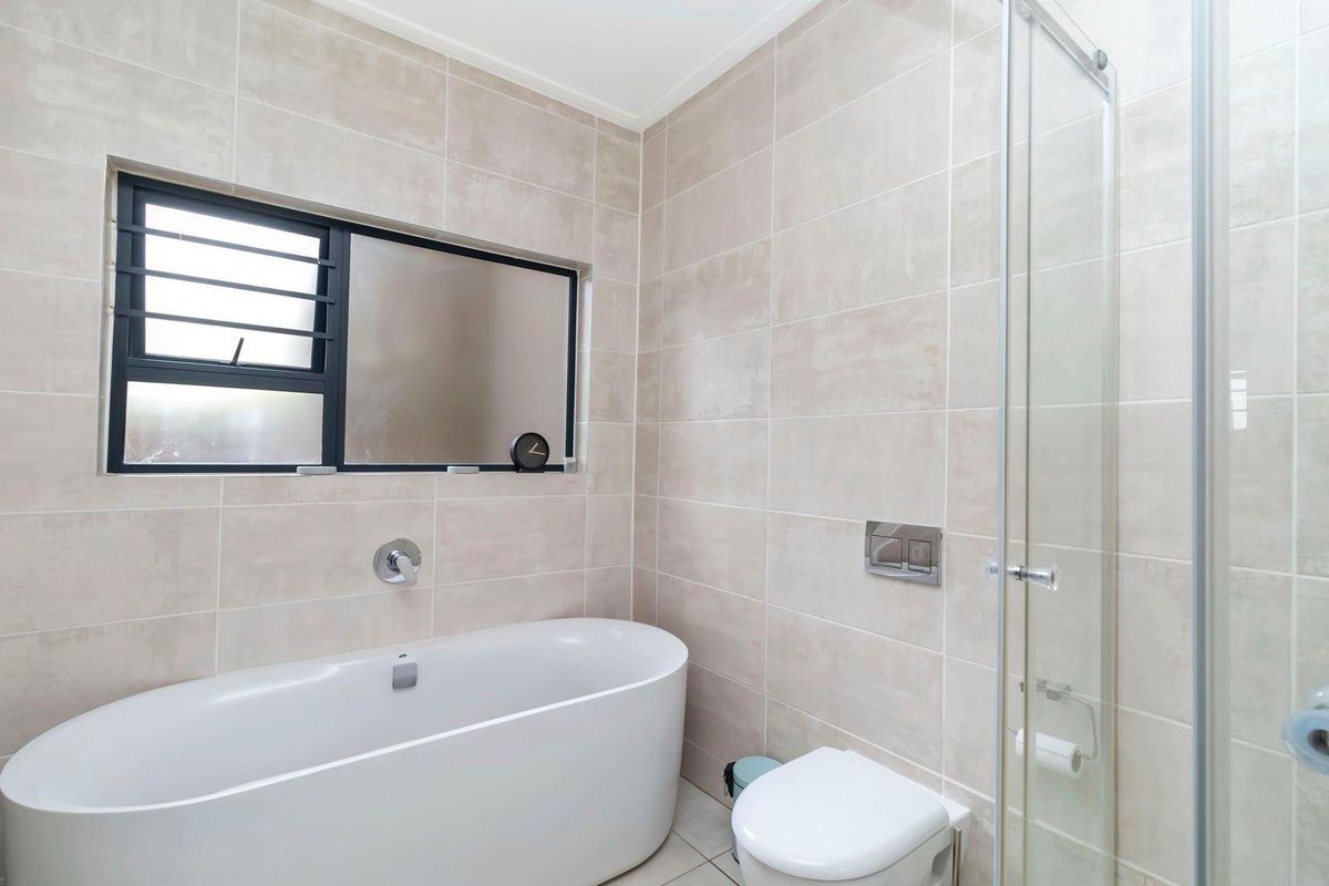 Modern bathroom featuring a freestanding bathtub, a glass-enclosed shower, and a wall-mounted toilet with neutral floor-to-ceiling tiling.
