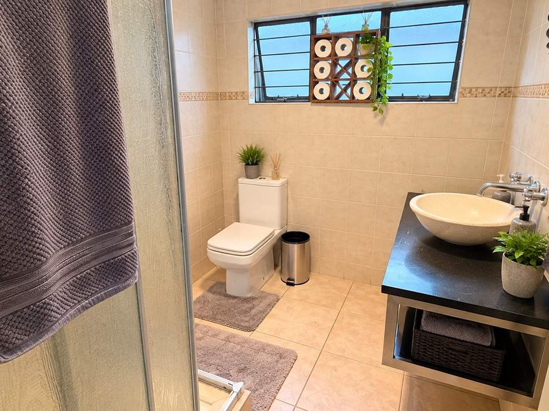A well-maintained bathroom featuring a shower enclosure, a modern vessel sink on a vanity countertop, and neutral wall and floor tiling.