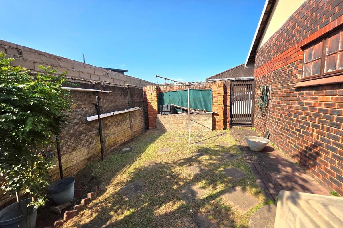 A private rear courtyard featuring a brick boundary wall, paved walkway, and small lawn area with a side gate access.