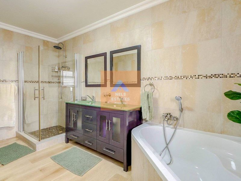 Modern bathroom featuring a glass-enclosed shower, a dark wood vanity with double mirrors, and a separate bathtub with tiled wall finishes.